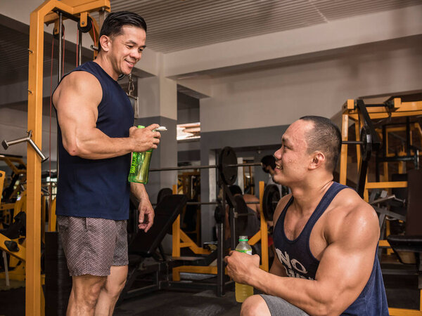 Two bodybuilders have a friendly chat after a workout session. Both holding a post workout drink.