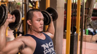 Filipinli formda bir adamın Dumbbell Shoulder Presses 'ı çekerken yakın çekimi. Alıştırma ya da çalışma deltleri.