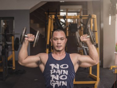 Kaslı ve kaslı bir Asyalı spor salonunda talim yapıyor. Oturan Omuz Dumbbell Baskıları Örneği.