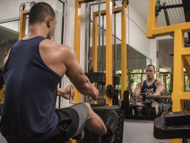 Formda ve atletik Asyalı bir adam V-Bar ile kablolu yaylı sıra yapıyor. Sıkı bir spor salonunda antrenman yapıyorum..