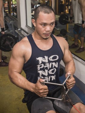 Formda ve atletik Asyalı bir adam V-Bar ile kablolu yaylı sıra yapıyor. Sıkı bir spor salonunda antrenman yapıyorum..