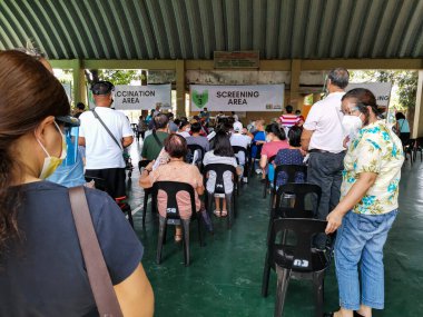 Las Pinas, Metro Manila, Filipinler - Nisan 2021: Aşı alanı olarak kullanılan basketbol sahası. Yüz maskeleri ve yüz kalkanları olan insanlar, anti-Covid-19 aşısı için sıralarını bekliyorlar..