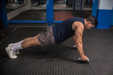 Atletik bir adam kauçuklu zeminde şınav çeker. Yan görüş. MMA spor salonunda HIIT ya da jimnastik.