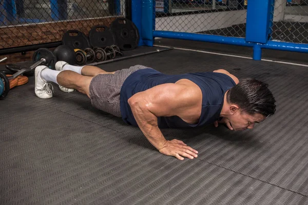 Atletik bir adam kauçuk kaplı zeminde normal şınav çeker. MMA spor salonunda HIIT ya da jimnastik.