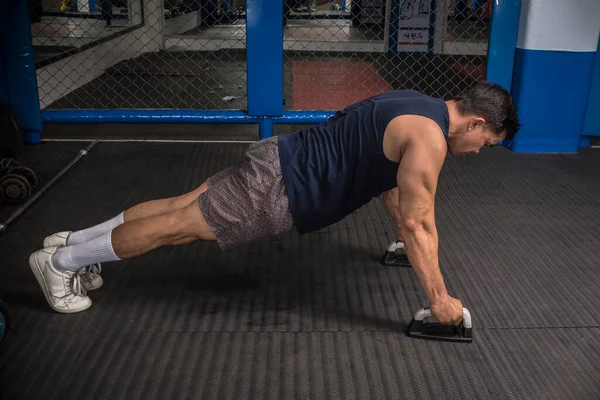 Atletik bir adam kauçuklu zeminde şınav çeker. Yan görüş. MMA spor salonunda HIIT ya da jimnastik.