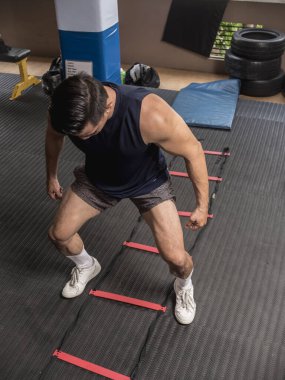 Yakışıklı Asyalı bir adam kapalı spor salonunda çeviklik merdiveniyle HIIT egzersizi yapıyor. Ayaklar meydanın dışında. Fitness rutini.