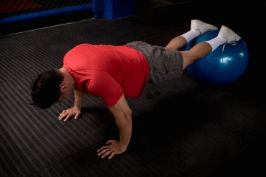 Atletik ve zinde bir Asyalı denge topunda şınav çeker. Karın ve çekirdek egzersizi ve egzersiz. Tepeden çekim.