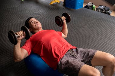 Yakışıklı ve formda Asyalı bir adam Stability Ball Dumbbell Göğüs Baskısı yapıyor. Spor salonunda ya da spor salonunda çalışıyorum..