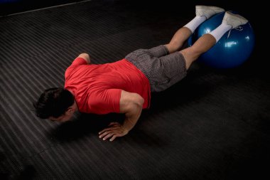 Atletik ve formda Asyalı bir adam dengeli top şınavı yapar. Karın ve çekirdek egzersizi ve egzersiz. Tepeden çekim.