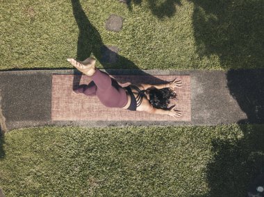 Asyalı bir kadının aşağı doğru köpek bacağı kaldırışının en üst görüntüsü. Vücut ağırlığı egzersizi. Bir parkta ya da evin bahçesindeki patikada yoga..
