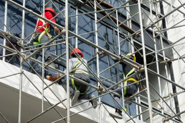 İnşaat işçileri midrise ofis binasının dış cephesinde son işleri yapıyorlar - boyama ve cam döşeme -.