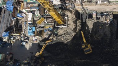 Yüksek bir binanın şantiyesi. Temel çalışmaları, kazıcılarla yapılan toprak çalışmaları ve bir kule vinci. Başka bir gökdelenden aşağıya bakıyor..