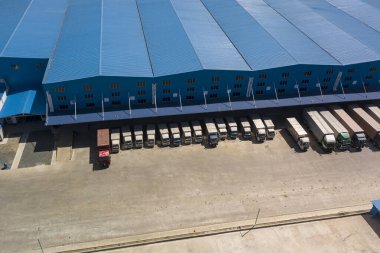 Büyük mavi bir depoya ya ya da lojistik merkezine park etmiş ya da boşaltmış bir sürü tırın havası. Lojistik ve dağıtım konsepti.