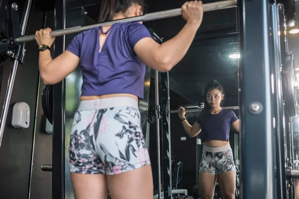 A determined young asian female does leg squats at the smith machine.