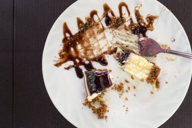 Siyah bir masada kısmen yenmiş yaban mersinli cheesecake tabağı. Arta kalan tatlıyı seç.