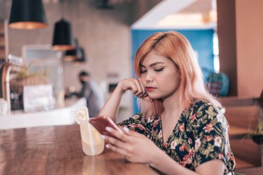 Genç bir Asyalı kadın gelen kutusunu kontrol ediyor, erkek arkadaşının geç kaldığı için mazeretini görüyor, açıkça onu rahatsız ediyor. Moda olan bir kahve dükkanında ya da kafede. Limonata sipariş ettim..