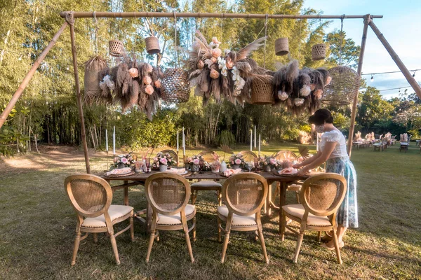 A wedding stylist or organizer prepares a bride and groom table. Open-air banquet, a rustic garden ceremony reception.