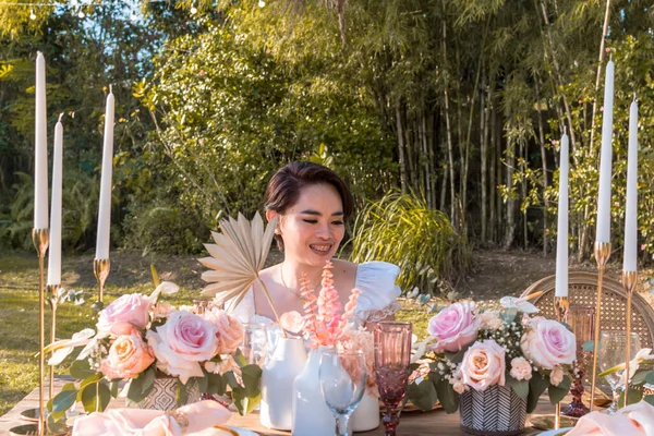 A young asian wedding stylist or organizer inspects an intricate rustic dining setup meant for a garden wedding ceremony.