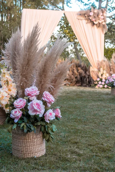A basket with dried pampas leaves and pastel pink roses. Decor for an aisle of a rustic garden wedding ceremony.