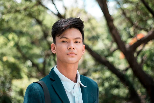 A handsome and young Filipino college student in smart casual wear. Serious look. At the park or campus grounds.