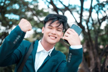 Elleri havada, Asyalı genç ve mutlu bir adam başarılı bir jest yaptı. Sınavı geçmek, okulda iyi notlar almak, kredi onayı almak ya da işe kabul edilmek. İyi haber konsepti.