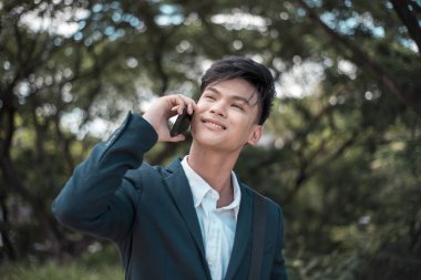 Genç ve kendinden emin bir girişimci dışarıda yürürken iş arkadaşları, müşterileri veya arkadaşlarıyla cep telefonuyla gelişigüzel konuşur. Genç yaşta başarılar. Park ya da doğa geçmişi.