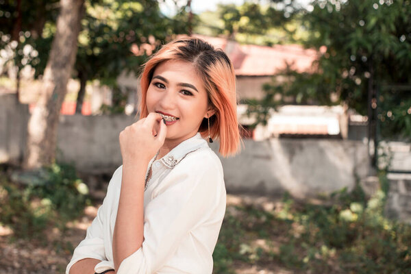 A young attractive and pretty southeast asian woman with strawberry blonde hair and medium length hair. Casual wear at the park.