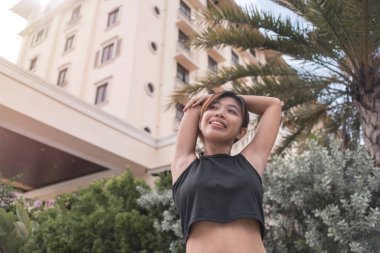 Siyah ekin bluzlu mutlu ve neşeli genç bir bayan koşmadan önce vücudunun üst kısımlarını gerer. Otel ya da konut geçmişi.