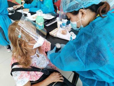 Las Pinas, Metro Manila, Filipinler - Haziran 2021: PPE kıyafetli bir sağlık çalışanı COVID-19 aşısı olmadan önce yaşlı bir vatandaşın kan basıncını kontrol ediyor.