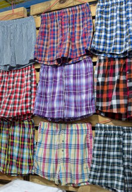 Duvarda asılı çeşitli ekose boxer şortlar. Pazar yerinde ya da butikte satılık erkek iç çamaşırları..