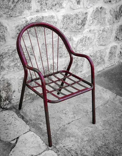 Old red metal chair beside stone wall, Montenegro