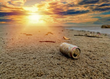 Gün batımında gökyüzü ve çevre kirliliği kavramlarıyla sahilde çöplüğe dönüşen kullanılmış içecek..