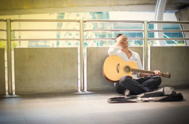 İşsiz bir adam umutsuz hisseder. Beyaz bir gömlek giyiyor, üst geçitte oturuyor ve gitar çalıp para istiyor. O bir dilenci oldu. İşsizlik stresi, Coronavirüs salgını konsepti.