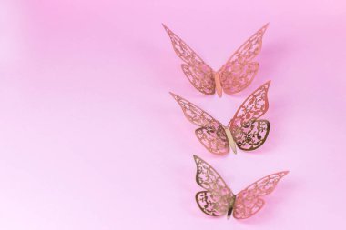 Pembe arka planda dekoratif altın renkli üç kelebek. Dekor. metin için yer