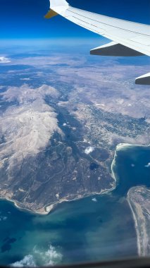 Mavi gökyüzüne ve beyaz bulutlara karşı yolcu penceresinden görülen uçan bir uçağın kanadı. Uçak penceresinden fotoğraf çekmek. İlk uçağa binmenin heyecanı.