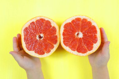 Çocuğun elinde yarım greyfurt, sarı arka plan