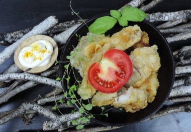 Dökme demir bir tavada kızarmış balık, sebzeler, otlar, sos, orijinal kırsal etno arka plan huş dalları ve siyah yüzey