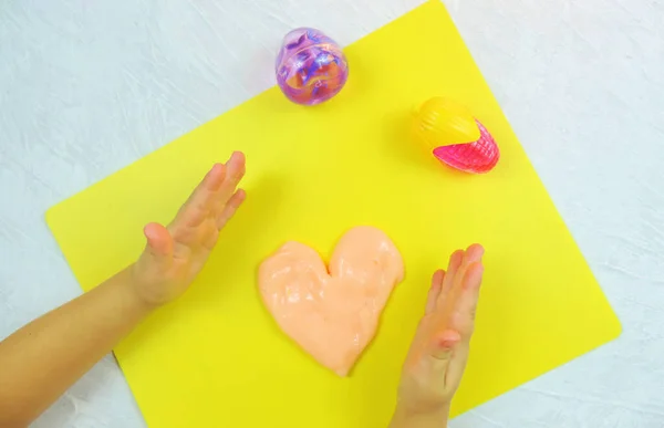 child\'s hands made funny heart from  slime , hammer slime,  yellow background