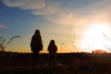       Gün batımında güzel bir gün batımının arka planında bir kadın ve bir çocuğun bulanık siluetleri.,    