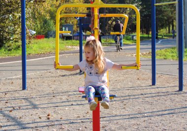 Oyun parkındaki küçük kız anaokulu öğrencisi spor için ve simülatörler üzerinde güç eğitimi için. Açık hava çocuk aktivitesi konsepti