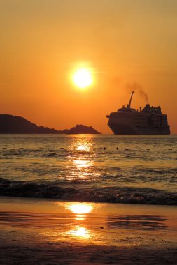 Gün batımında denizde siyah siluet yolcu gemisi uzakta.          