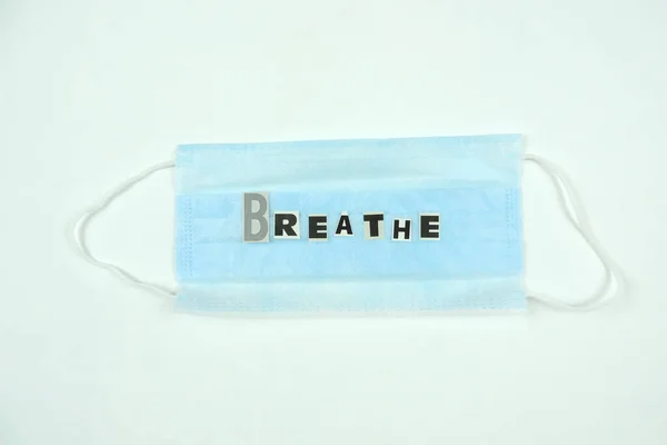 Medical blue disposable protective mask  and cut out letters composed word Breathe