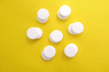 Beyaz askorbik vitamin tabletleri sarı arka planda çiçek şeklinde serili.