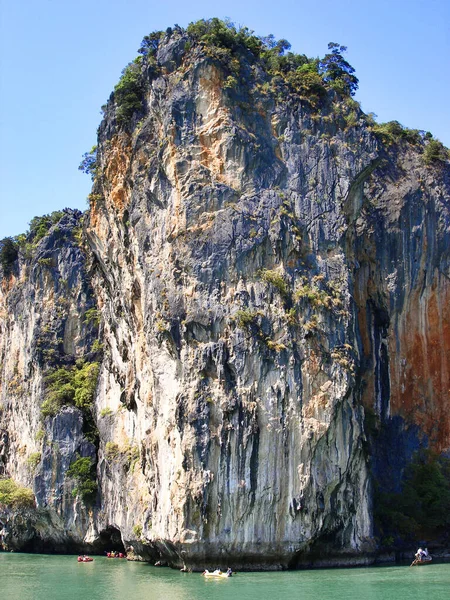 High sheer cliff with hanging cliffs of the mountain. tourists on inflatable boats at the foot of mountain