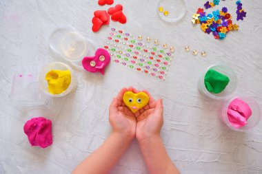 Çocuk renkli mankenlik kiliyle, boncuklarla, pullarla ve kalp figürleriyle oynuyor. Kil ile ev eğitimi oyunu. Erken kalkınma kavramı