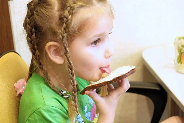 Little girl eating bread with butter lick sticking out tongue