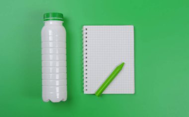 Beyaz plastik şişe ve yeşil zemin üzerinde kalem olan defter, maket yap, boşluğu kopyala          