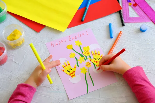 Child making card with Easter funny eggs and flowers  from colorful paper. Handmade. Project of children\'s creativity, handicrafts, crafts for kids. Happy easter inscription
