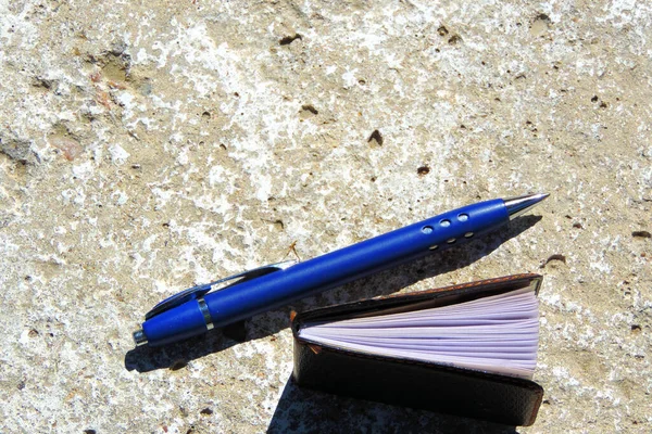 Μπλε Στυλό Και Μαύρο Σημειωματάριο Στην Επιφάνεια Του Σκυροδέματος Επίπεδη — Φωτογραφία Αρχείου