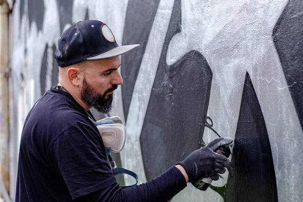Graffiti artist in action, drawing on the wall with aerosol spray paint in a can, wearing protective gloves. Street art culture concept.